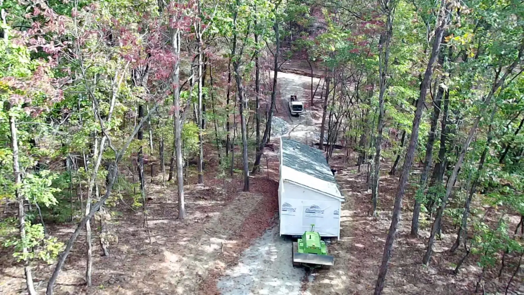 Aerial manufactured home delivery wooded road.